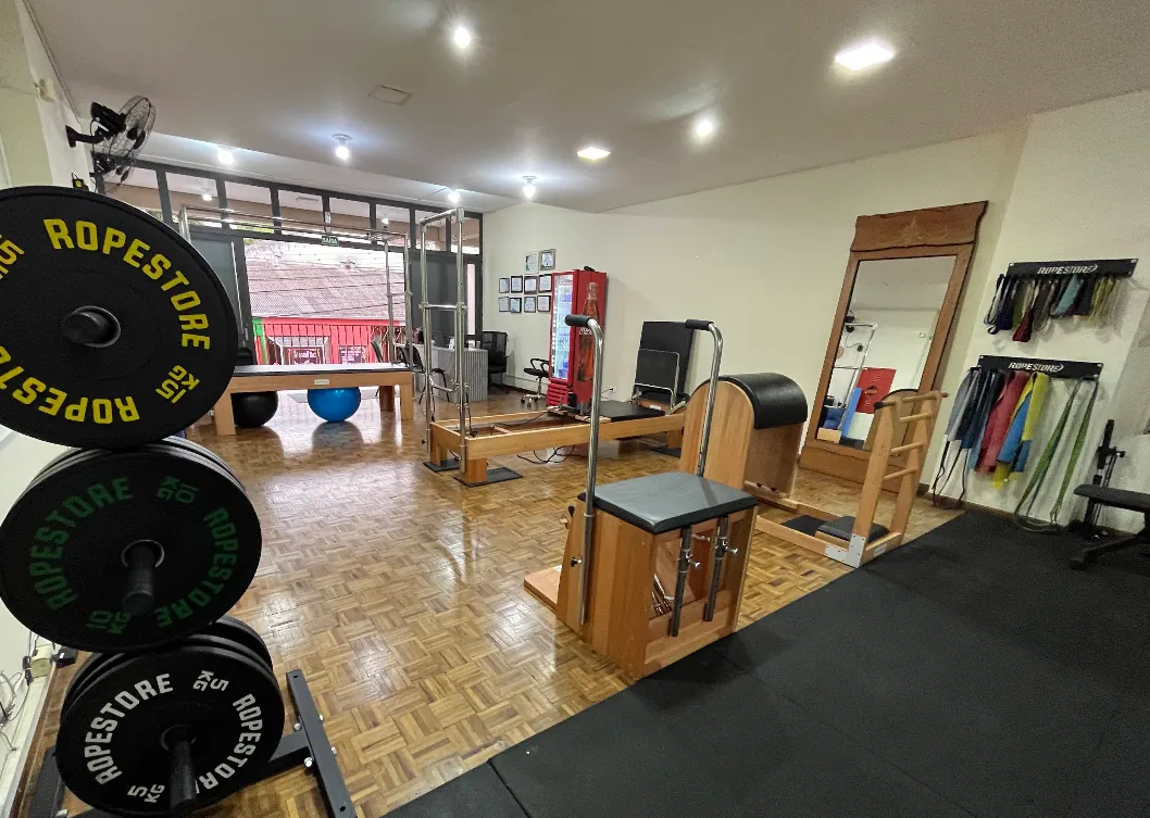 Estúdio com aparelhos de Pilates, espelhos e anilhas olímpicas